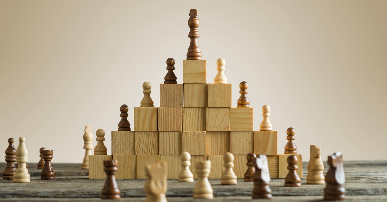 Chess pieces are arranged on wooden blocks in a pyramid shape, illustrating an advanced tax strategy: the pawns form the base while the king claims the top position.