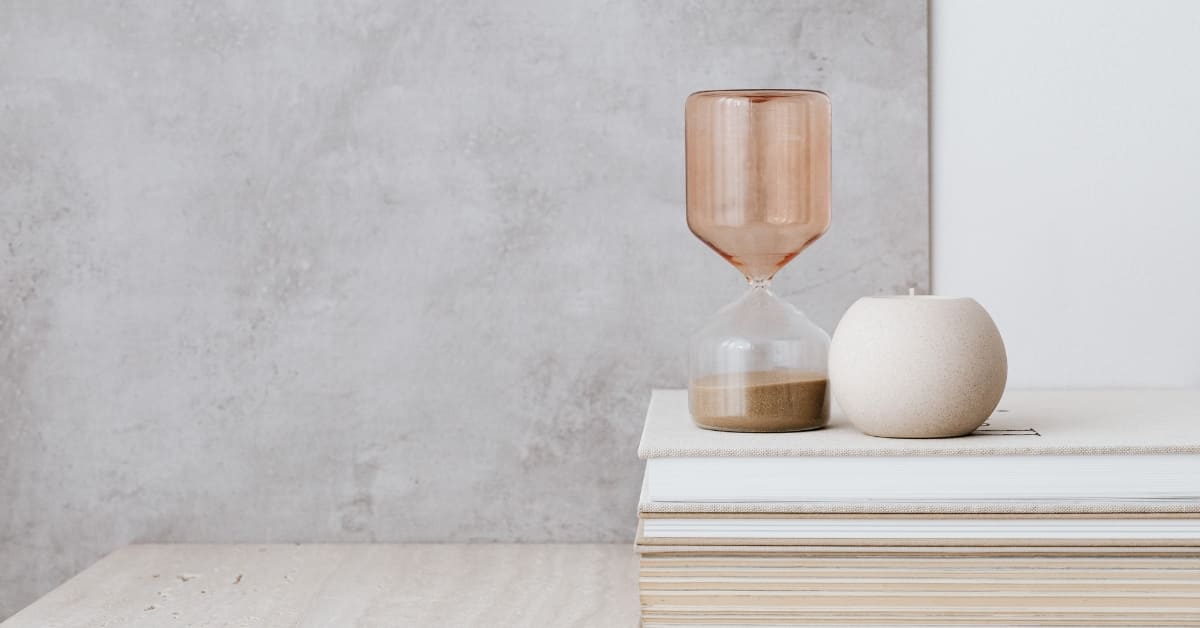 Proactive Tax Planning for High Earners (1) A pink hourglass and a beige candle sit on top of stacked books against a grey wall, symbolizing the importance of proactive tax planning for those seeking to stay ahead financially.