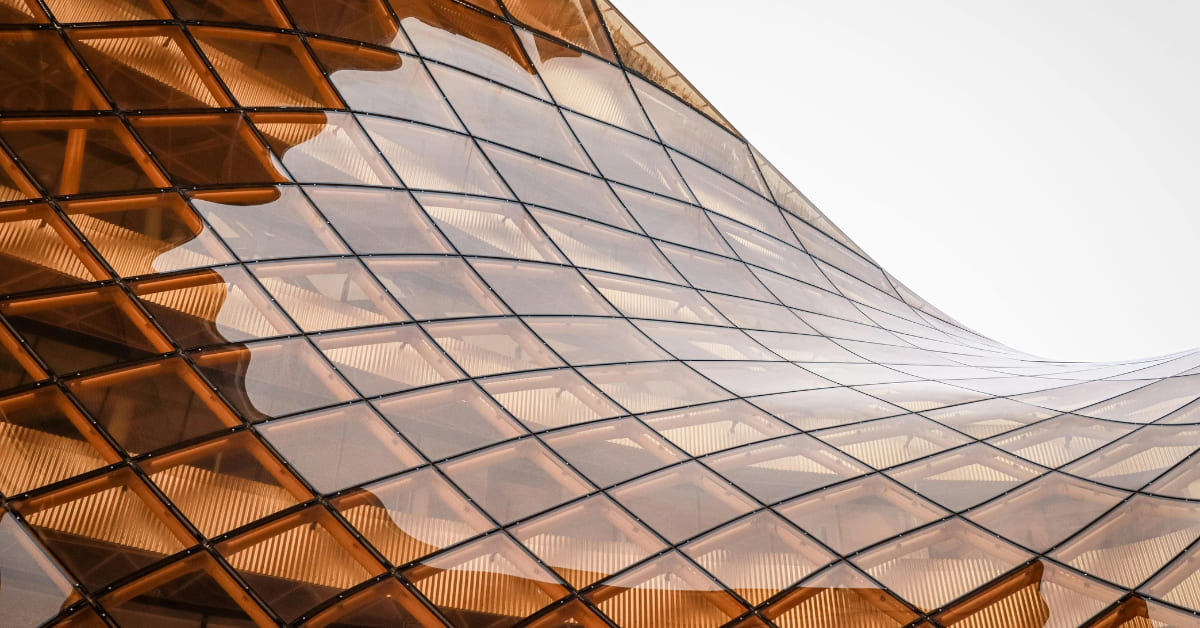 Curved, modern glass and metal architectural structure with a grid pattern against a light sky background—perfect inspiration for investors exploring short-term rental tax strategy opportunities.