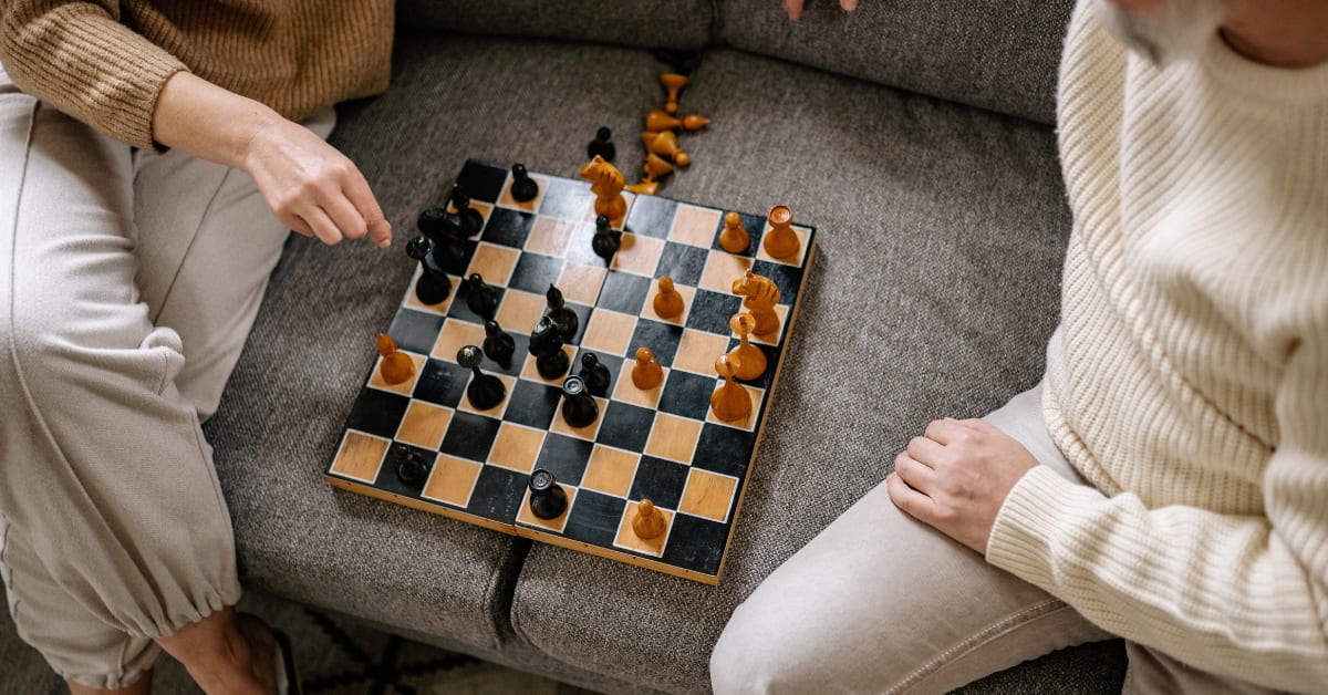 Two people sit on a couch playing a game of chess on a board between them.