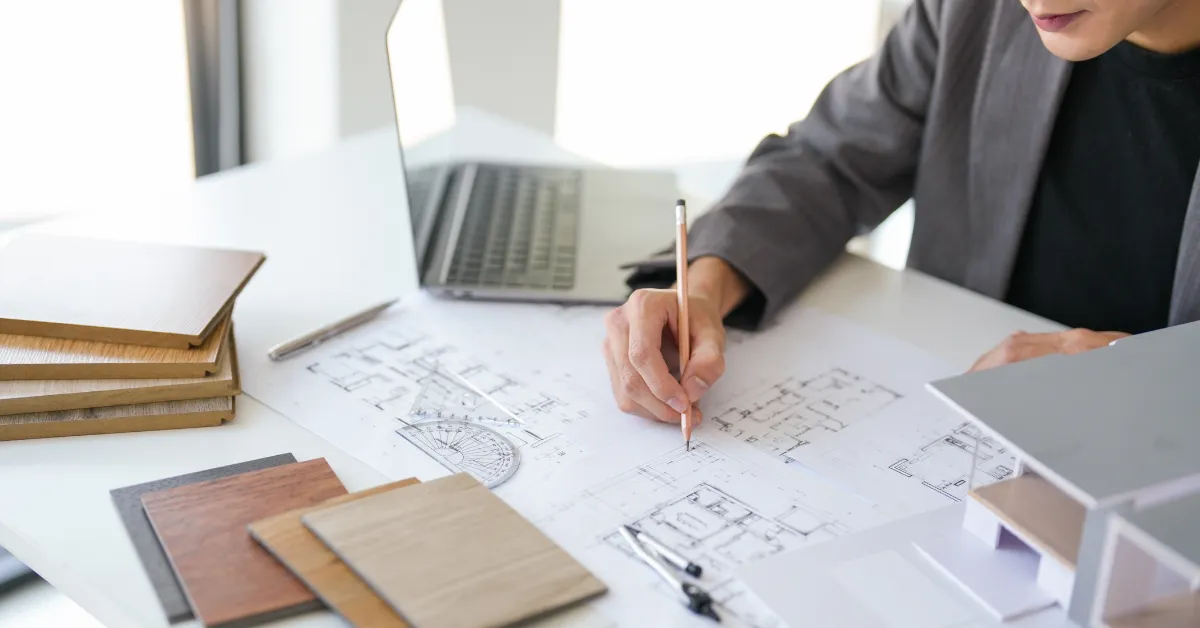Architect reviewing building plans with design samples and a laptop on a desk.