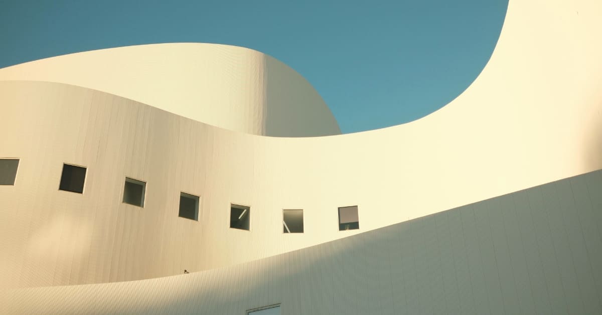 Modern curved architectural building with minimalist design, featuring smooth white walls, geometric windows, and open sky above.